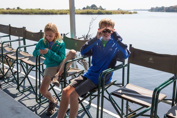 Tyler and Kara sitting on canvas chairs on a boat tour along the Chobe River.