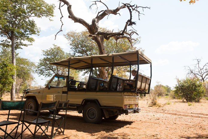 A parked Safari truck with open sides, a canopied rooftop, and four rows of seats.