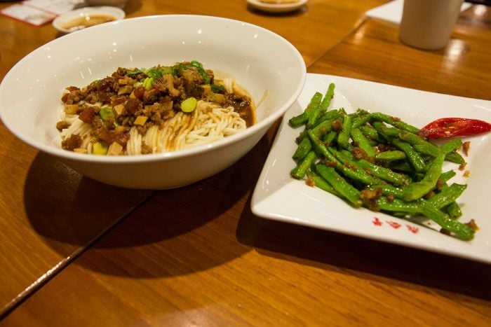 A bowl of noodles with toppings and a side plate of cooked green beans.