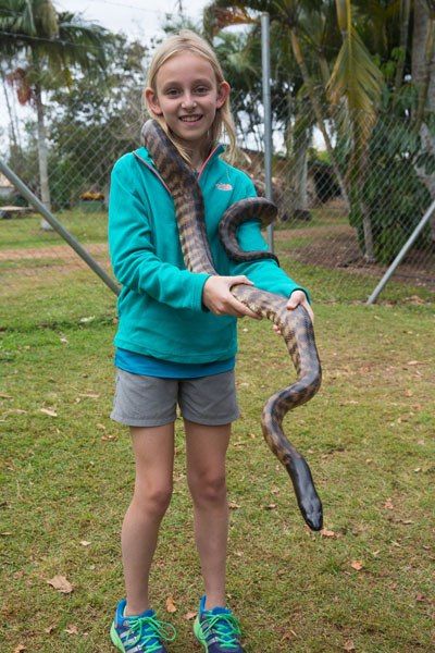 Kara stands and smiles with a large snake draped around her neck. She holds the snake's upper body in both hands.