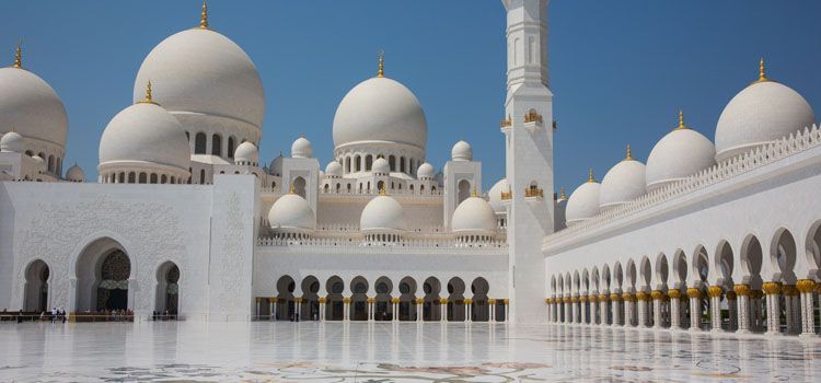 a large white building with domes and columns with Sheikh Zayed Mosque in the background