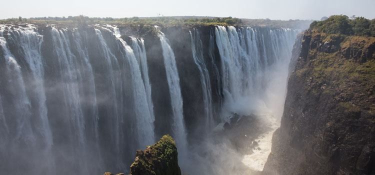 a large waterfall with water falling with Victoria Falls in the background