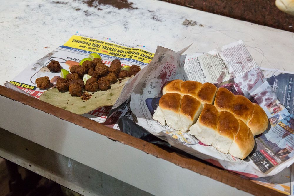 Mumbai meatballs made from beef and spices, served on newspaper with bread rolls.