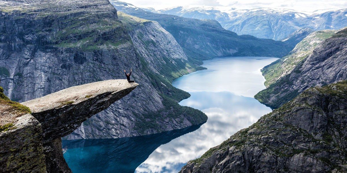 a person sitting on a cliff edge with a body of water in the background