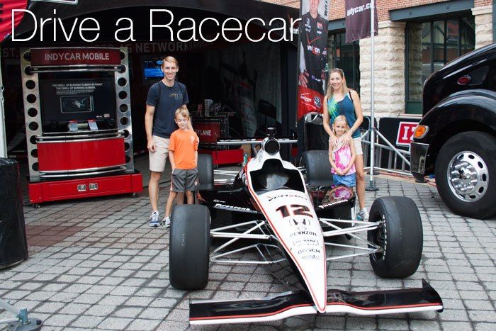 A family of four with a racecar in front.