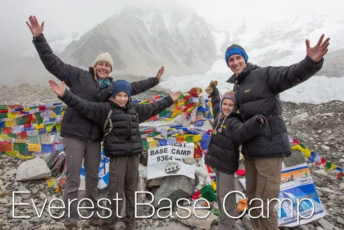A family of four waves at the camera at the Mount Everest Base Camp with snow in the background.