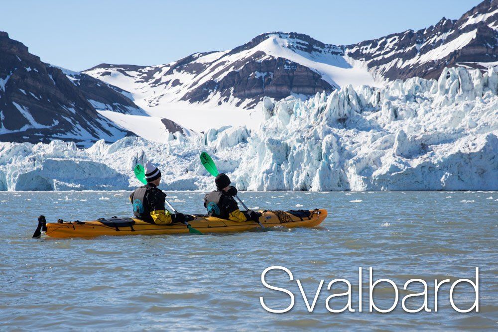 A couple of men kayaking with snow-capped mountains in the background in Svalbard, Norway.
