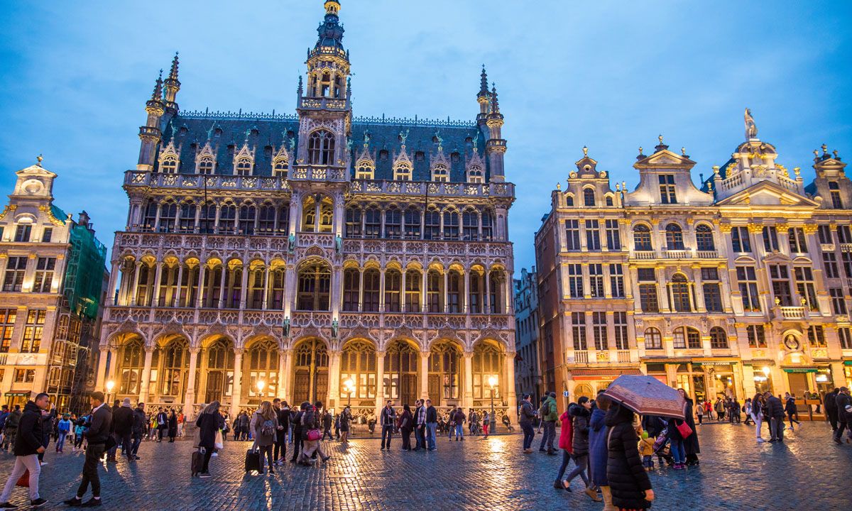 a group of people walking in a plaza with buildings with Grand Place in the background