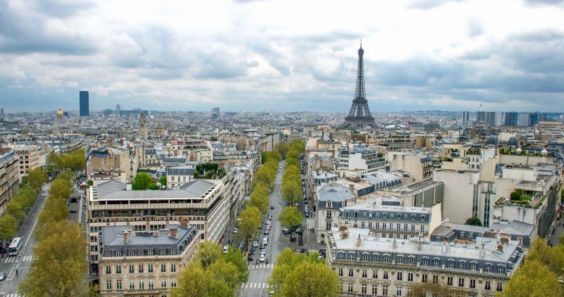 A view from a high vantage point of the Eiffel Tower with surrounding buildings and tree-lined streets leading up to it.